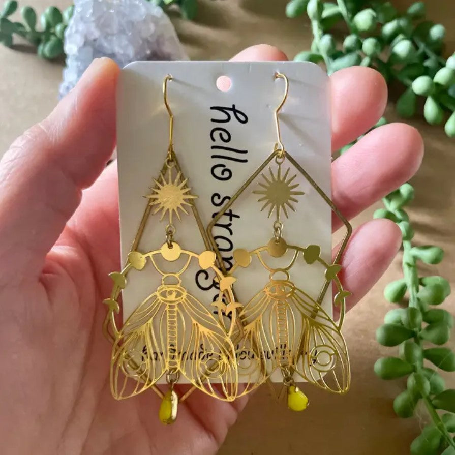 Gold dangle earrings in the shapes of large moths with folded wings surrounded by a ring of moon phases
