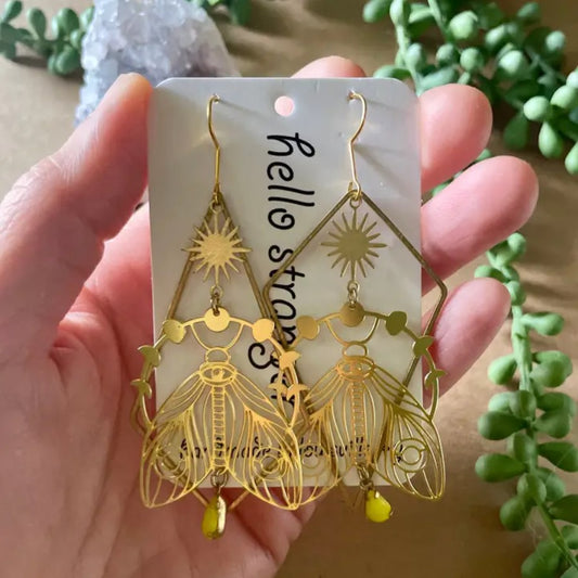 Gold dangle earrings in the shapes of large moths with folded wings surrounded by a ring of moon phases