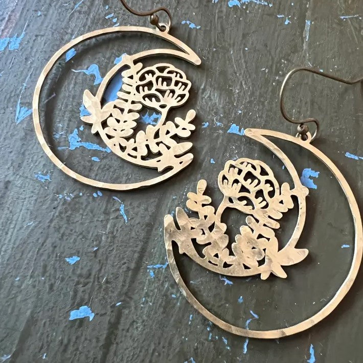 Dangling earrings in the shape of a cutout crescent moon with flowers blooming from it