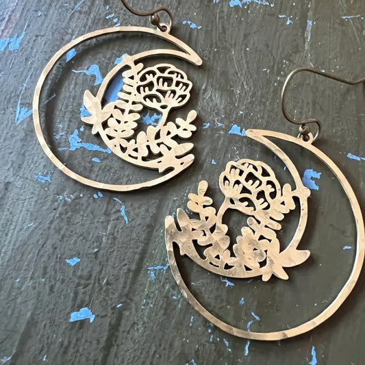 Dangling earrings in the shape of a cutout crescent moon with flowers blooming from it