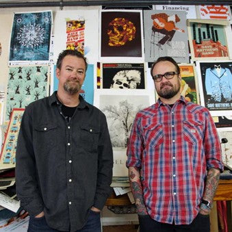 Robert and Mark, the artists of Methane Studios, standing before a wall of their work