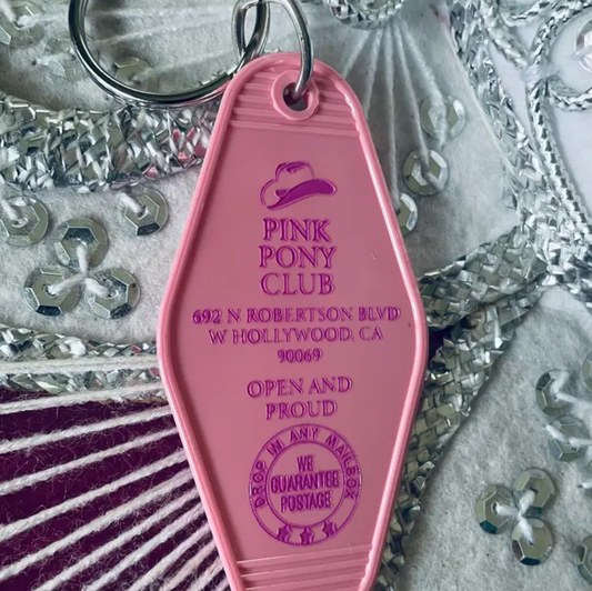 Pink keychain that reads "Pink Pony Club" followed by the address and the words "Open and Proud"