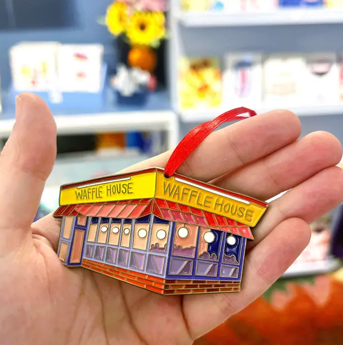 Person holding a metal Christmas ornament in the shape of a Waffle House restaurant