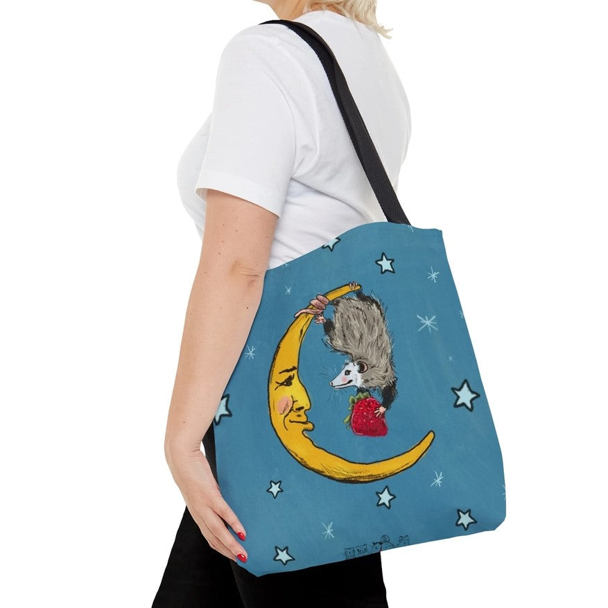 Tote bag with a possum holding a strawberry hanging off a moon with a face