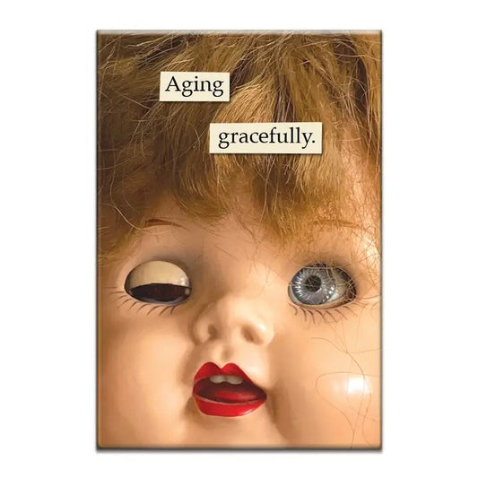 Magnet featuring a photo of a vintage doll head with straggly hair and one eye closed and the caption "Aging gracefully."