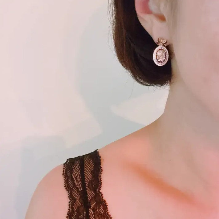 Pair of black and gold earrings shaped like framed roses hanging from bow-shaped studs