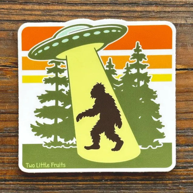 Sticker depicting a UFO capturing Bigfoot in a tractor beam in green, yellow and orange colors