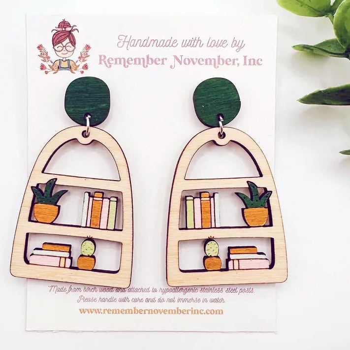 Wooden cutout earrings shaped like bookshelves with potted plants on them