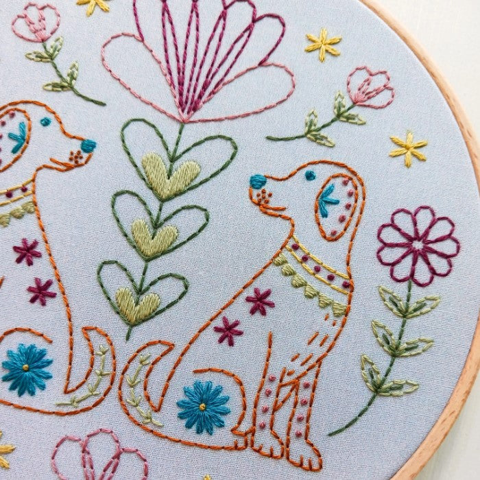 Closeup detail of embroidery hoop featuring two orange dogs surrounded by colorful flowers and plants