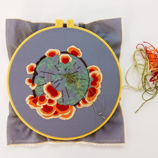 Embroidery kit with a design depicting wildflowers and fungus on a gray background