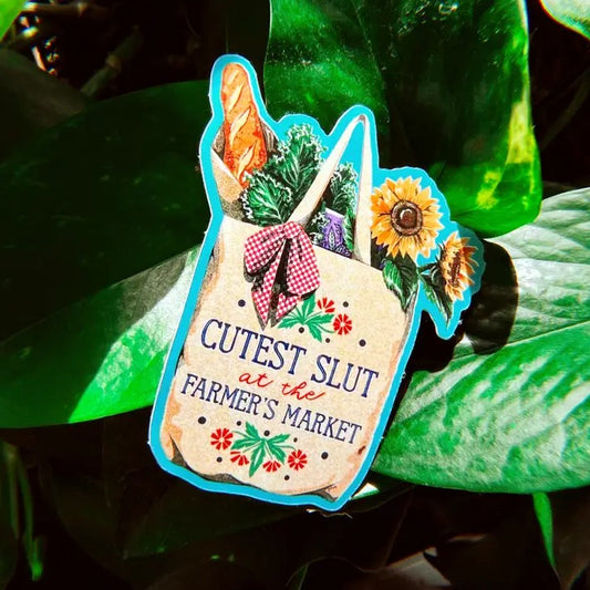 Sticker depicting an illustration of a tote bag filled with produce and sunflowers and bearing the caption "Cutest slut at the farmer's market"