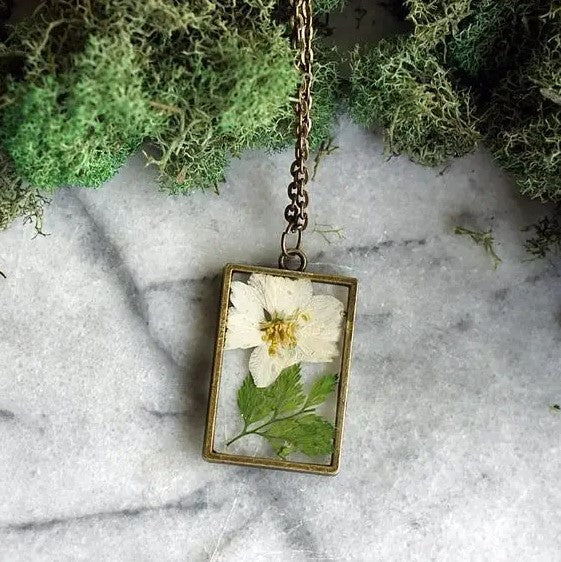 Necklace with a rectangular pendant that showcases a paperwhite narcissus flower in resin