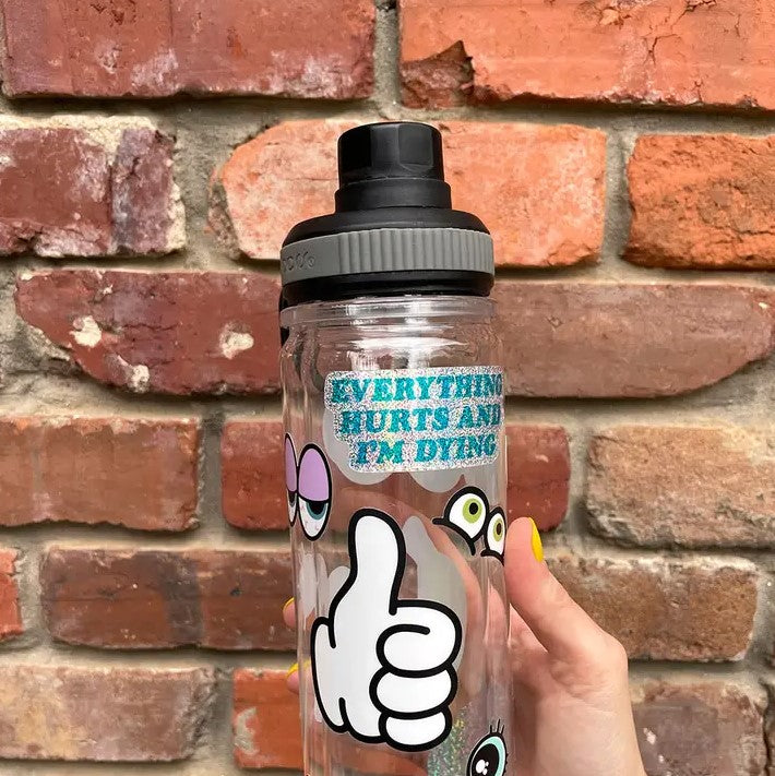 Silver glittery sticker that reads "everything hurts and I'm dying" in blue text; pictured on a water bottle