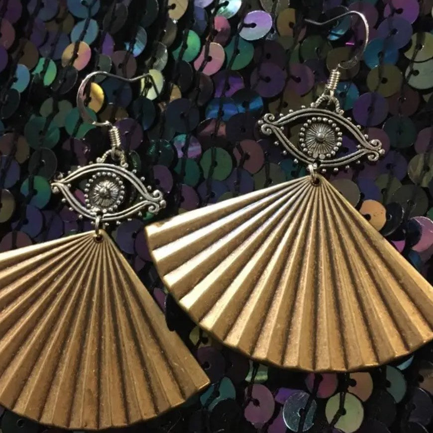Brass colored dangle earrings in the shapes of eyes with fans hanging under them