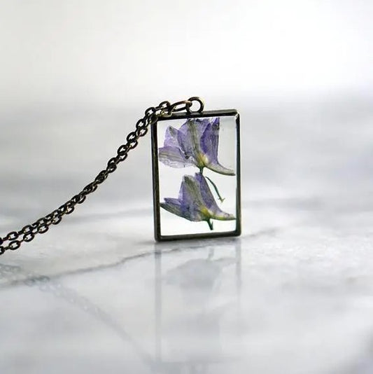 Necklace with a rectangular pendant that showcases an iris flower in resin