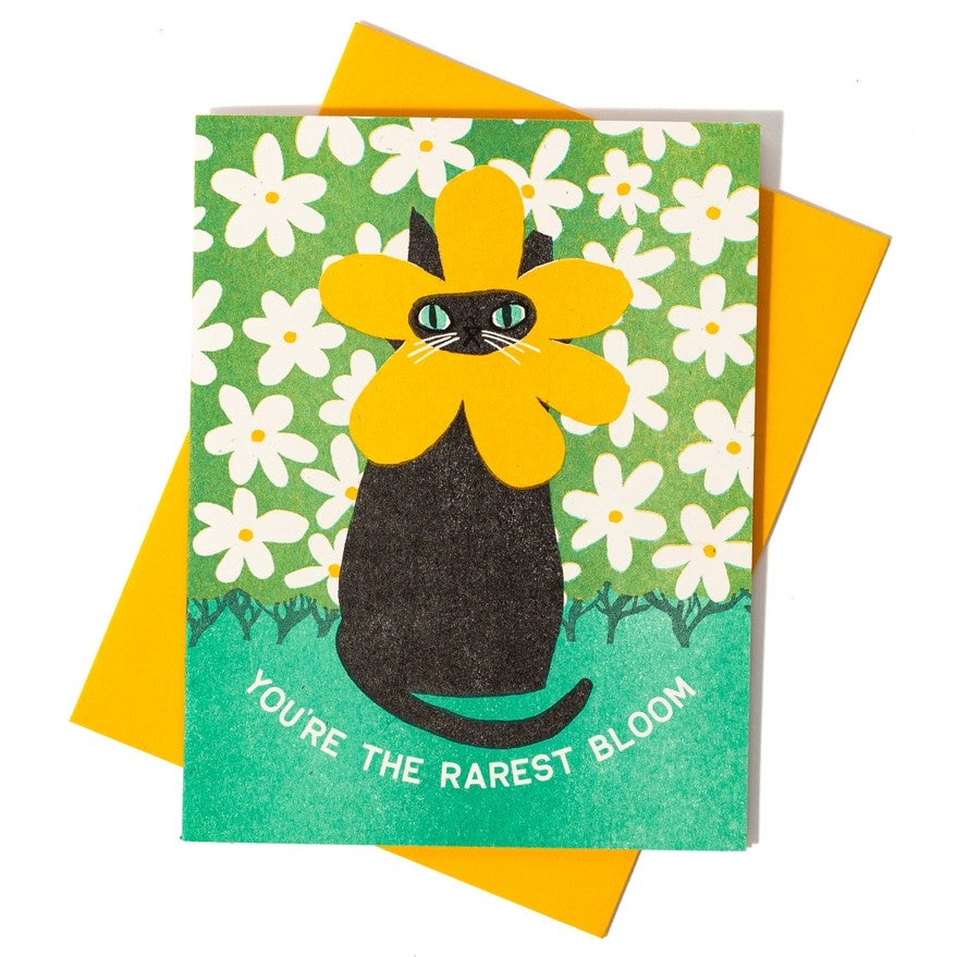 Greeting card featuring a black cat with yellow flower petals around its face and text reading "you're the rarest bloom"