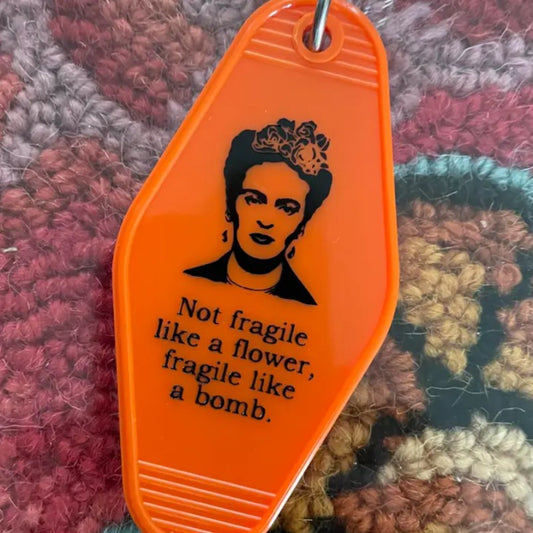 Orange keychain featuring an image of Frida Kahlo and the words "Not fragile like a flower, fragile like a bomb."
