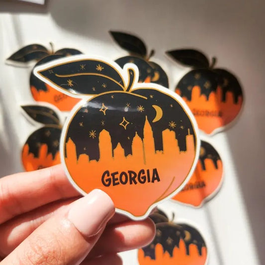 Small vinyl sticker shaped like a peach, depicting a black and orange Atlanta skyline