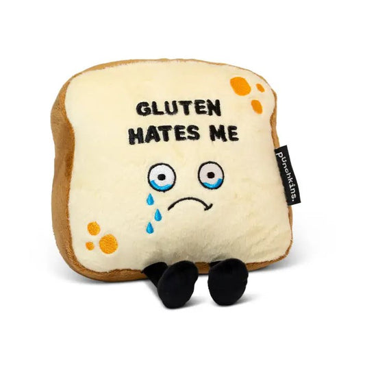 Plush toy in the shape of a piece of bread with a frowny face and tears in its eyes. The words "gluten hates me" are stitched on it