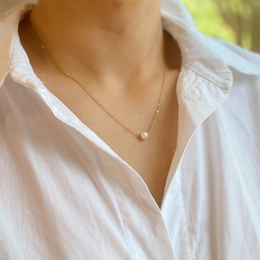 A necklace with a thin gold plated chain and a dainty single pearl bead pendant