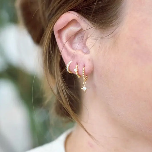 Small gold huggie earrings with a star shaped hanging charm