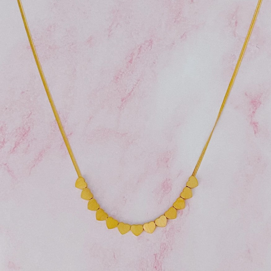 Gold necklace with a row of small delicate gold hearts at the center