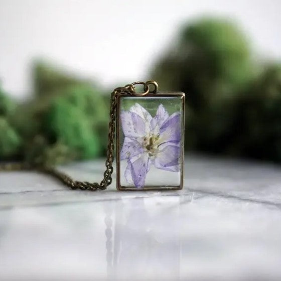 Necklace with a rectangular pendant that showcases a larkspur flower in resin