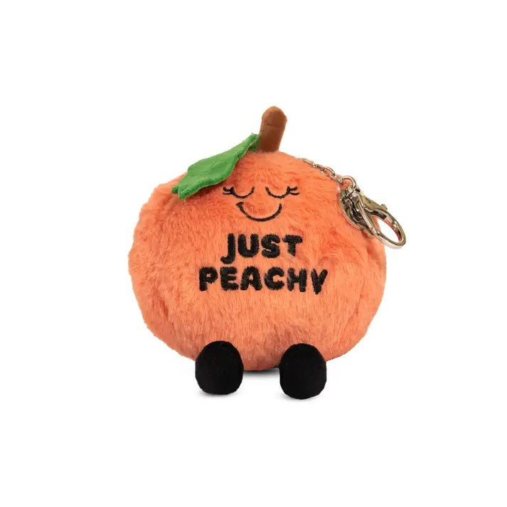 Peach plushie keychain with a peaceful smiling face and the words "Just Peachy" stitched on it in black thread