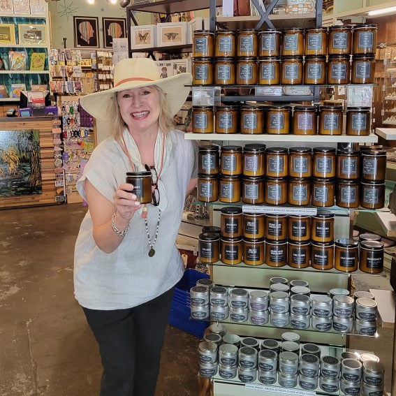 Artist of Kinfolk of Mine Candles holding a candle she made in front of her display of products