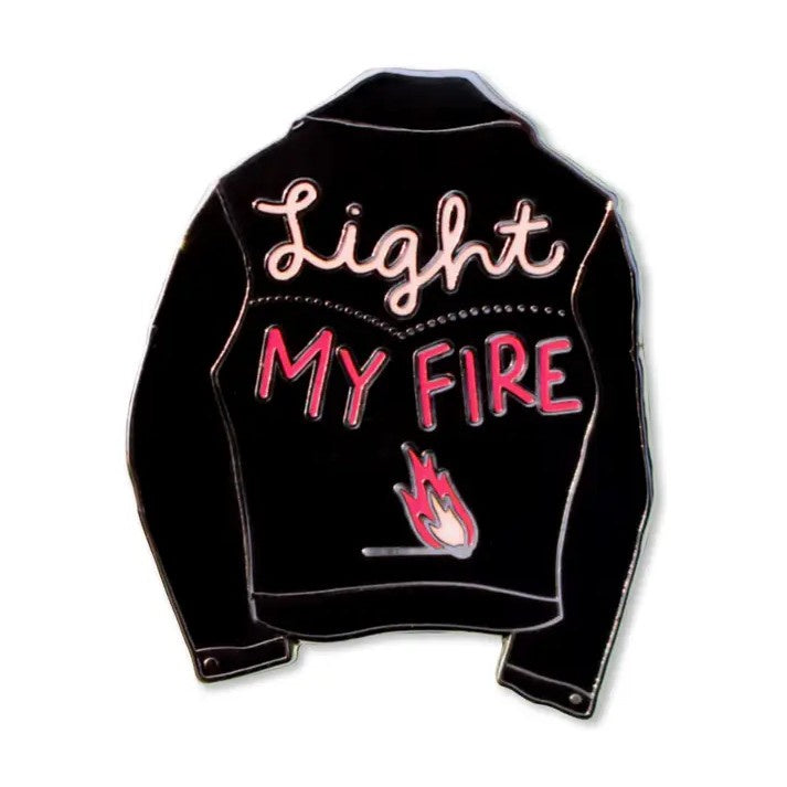 Enamel pin in the shape of a black leather jacket with the words "Light my fire" written in pink
