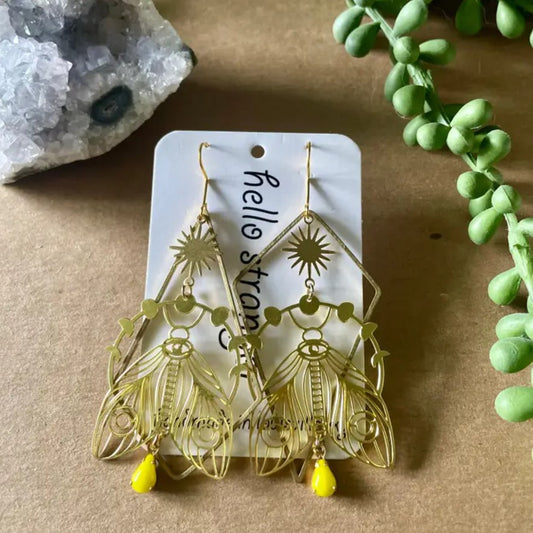 Gold dangle earrings in the shapes of large moths with folded wings surrounded by a ring of moon phases