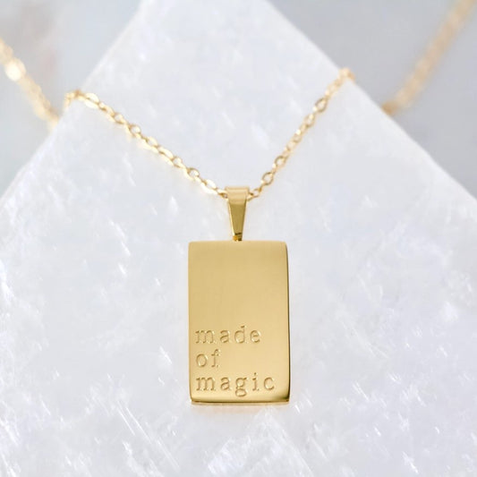 Gold necklace with small rectangular pendant inscribed with the words "made of magic"