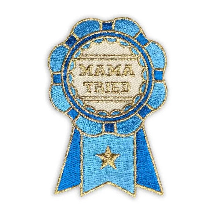 Embroidered fabric patch in the shape of a blue prize ribbon with gold text reading "Mama tried"