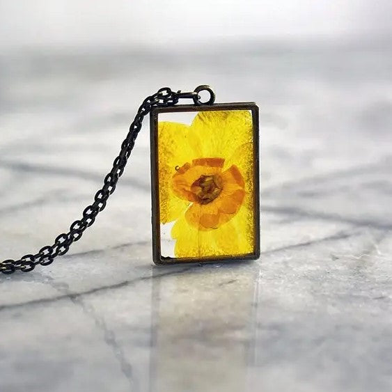 Necklace with a rectangular pendant that showcases a daffodil flower in resin