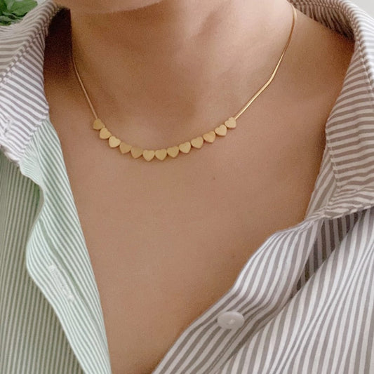 Gold necklace with a row of small delicate gold hearts at the center