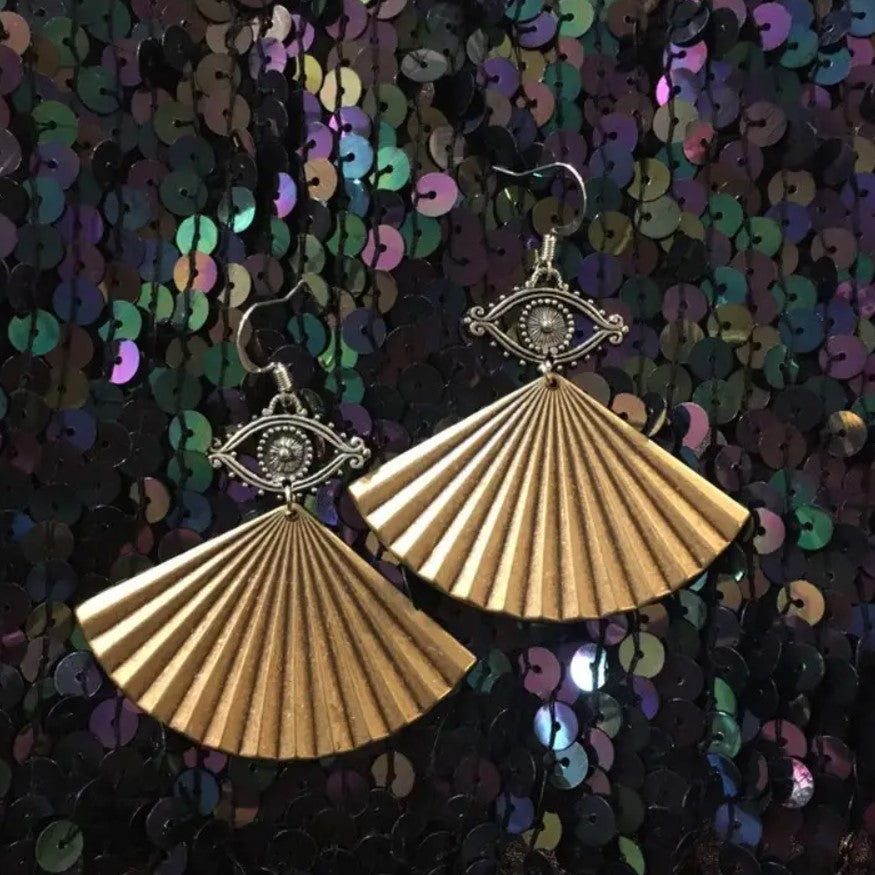 Brass colored dangle earrings in the shapes of eyes with fans hanging under them