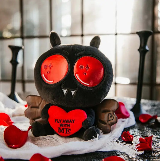 Black plush toy shaped like Mothman holding a heart that reads "Fly away with me"