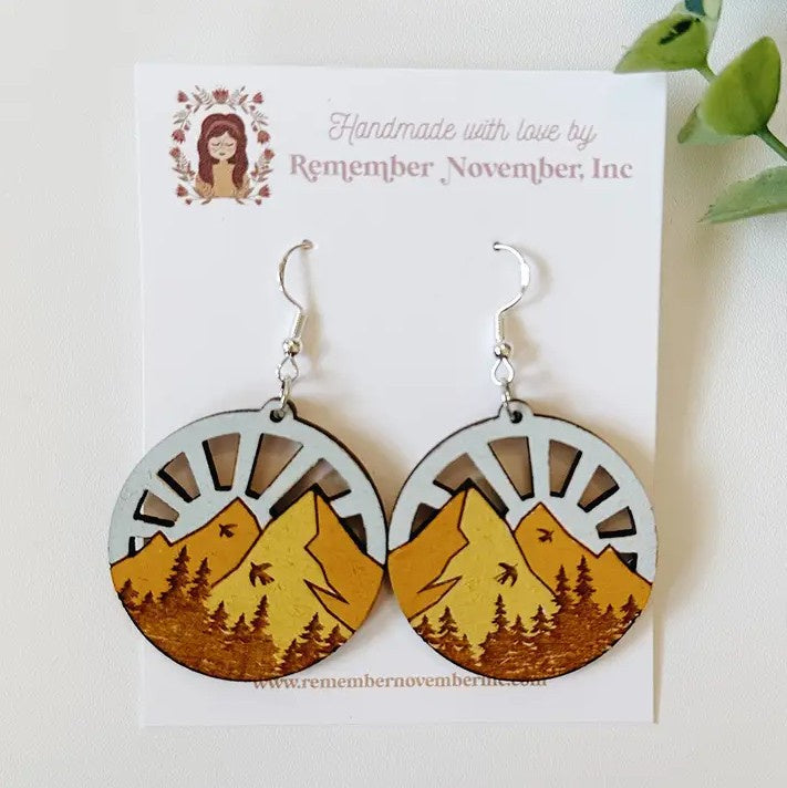 Circular wooden earrings depicting engraved birds flying over a mountain range