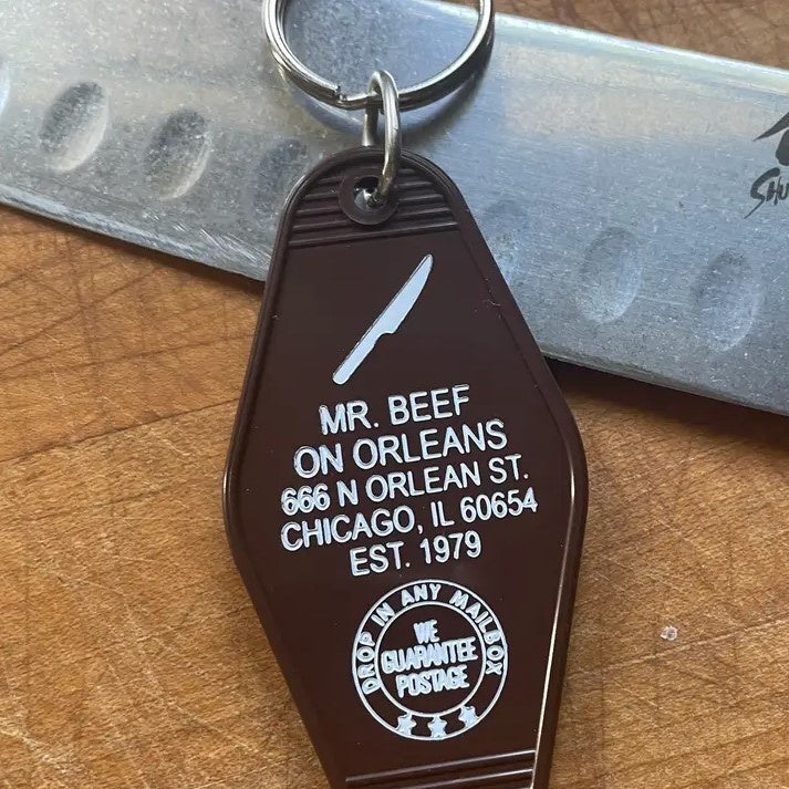 Dark brown keychain with a small image of a knife and the words "Mr. Beef on Orleans 666 N Orlean St. Chicago, IL 60653 Est 1979."