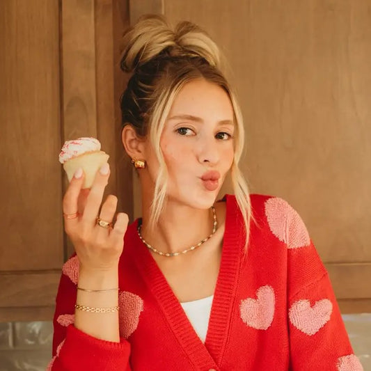 Woman in a red sweater with heart patterns holding a cupcake.