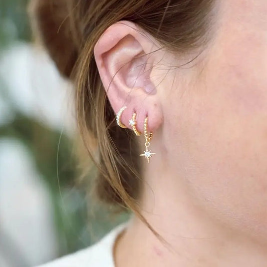 Closeup of a woman wearing three sets of gold earrings