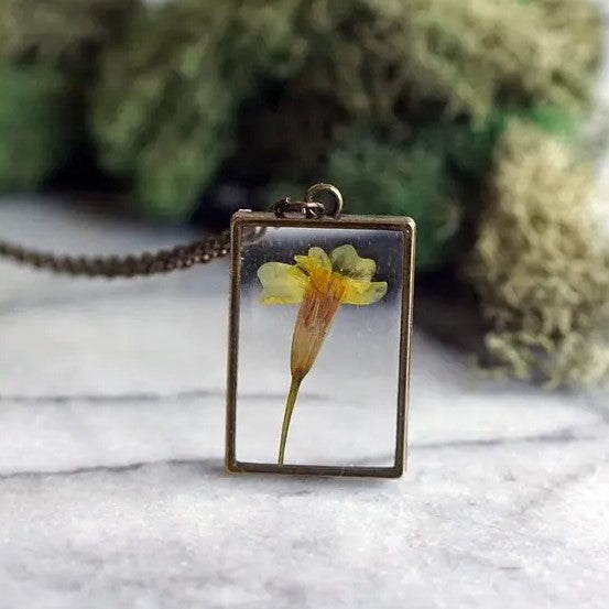 Necklace with a rectangular pendant that showcases a marigold flower in resin