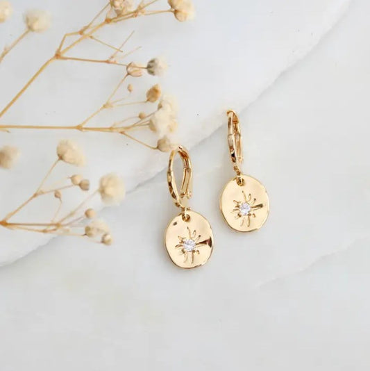 Delicate earrings with dangling gold circles etched with a small star and an opal gem at the center