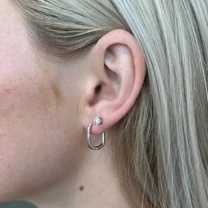 Closeup of an earing wearing a small silver oval hoop earring