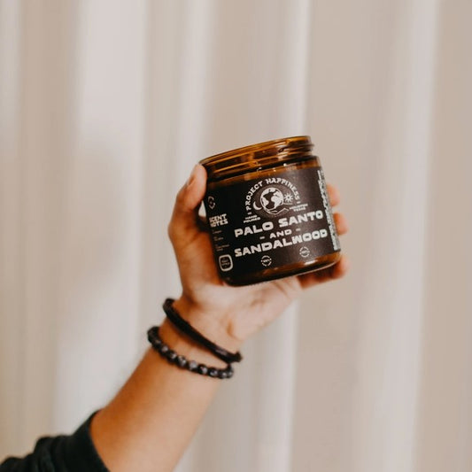 Hand holding a jar labeled 'Palo Santo and Sandalwood' against a neutral background