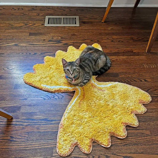 A brown tabby cat lying on a bright yellow shag rug shaped like a bowtie pasta