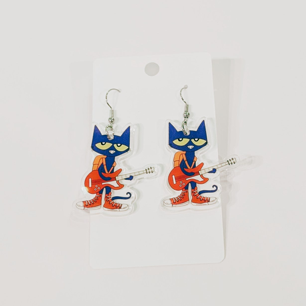 Earrings featuring Pete the cat, a blue cartoon cat with a red electric guitar, red sneakers and an orange backpack