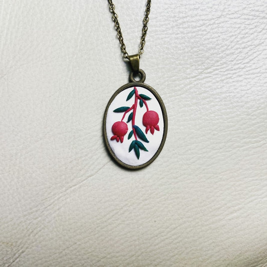 Chain necklace with a sculpted clay pendant depicting red pomegranates on a white background