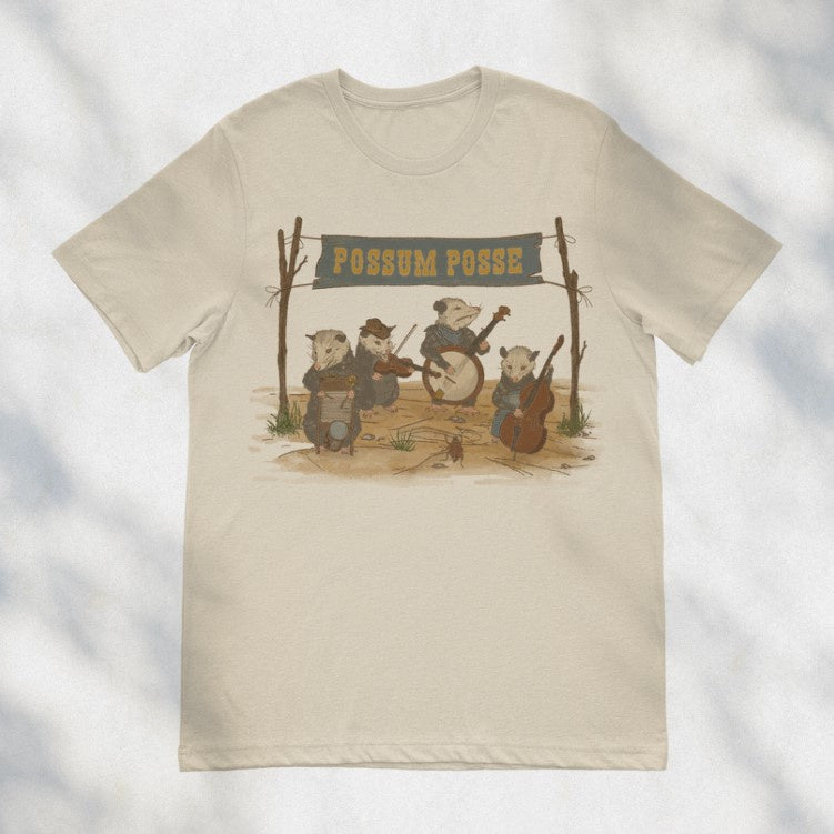 Beige tee shirt with an image of four possums in the desert playing in a country band, under a banner that says "Possum Posse"