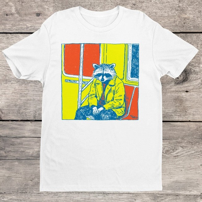 White t-shirt with a colorful graphic of a raccoon in a yellow jacket sitting on the subway